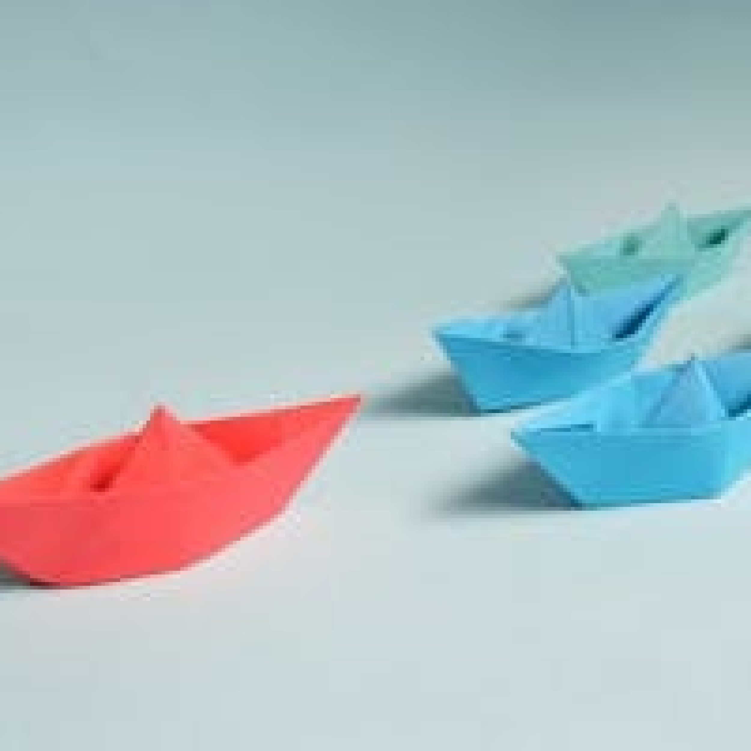 Colorful origami paper boats arranged to depict leadership and teamwork concepts.